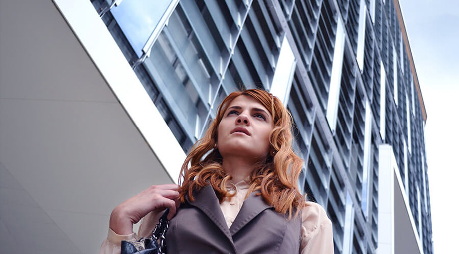 Assicurazioni Parametriche - Donna professionista con borsa guarda verso l'alto davanti a grattacielo moderno in vetro, ambiente business urbano